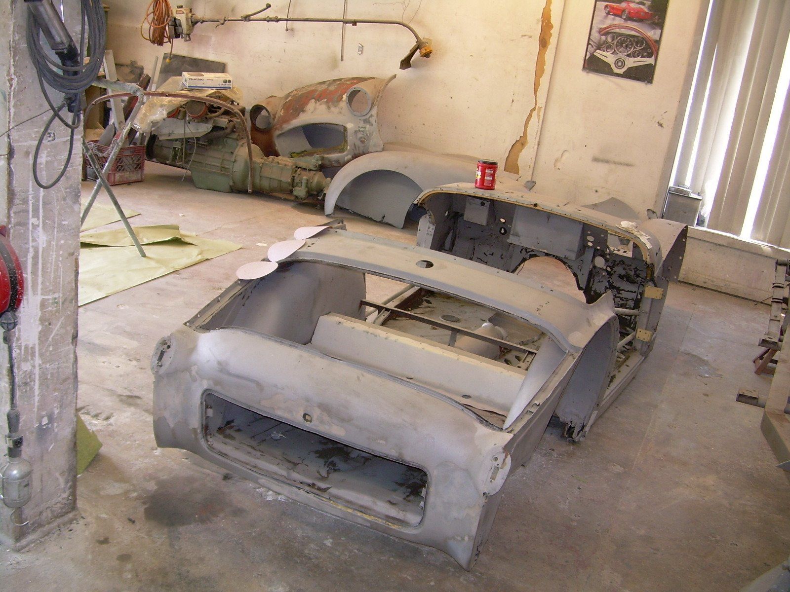Car restoration workshop with disassembled car body parts; gray, indoors.