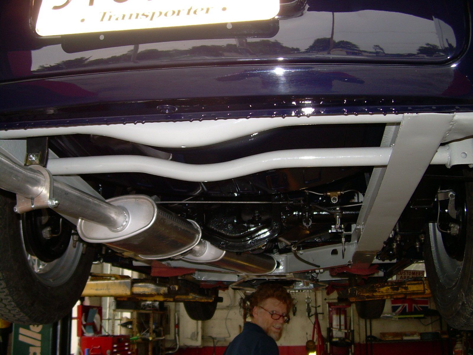 Undercarriage of a blue car. Exhaust pipes, white frame, and a person in a garage.