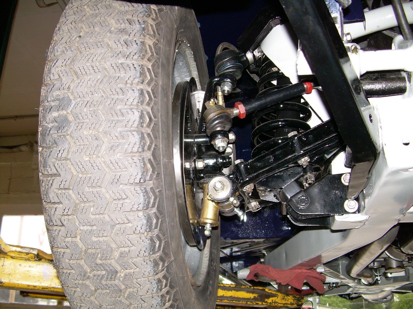 Close-up of a car's front suspension, wheel, and tire. Black and silver components on a raised vehicle.