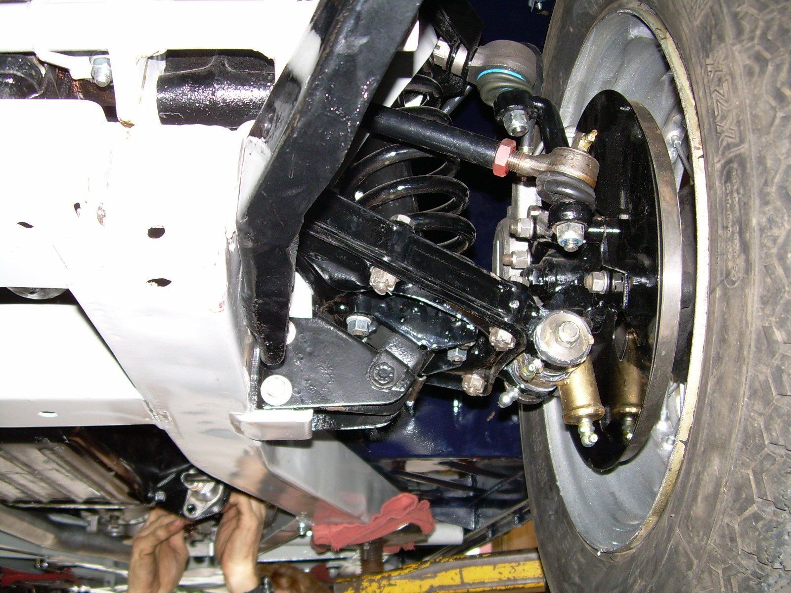 Undercarriage view of a black front suspension assembly with a wheel, tire, and metallic components.