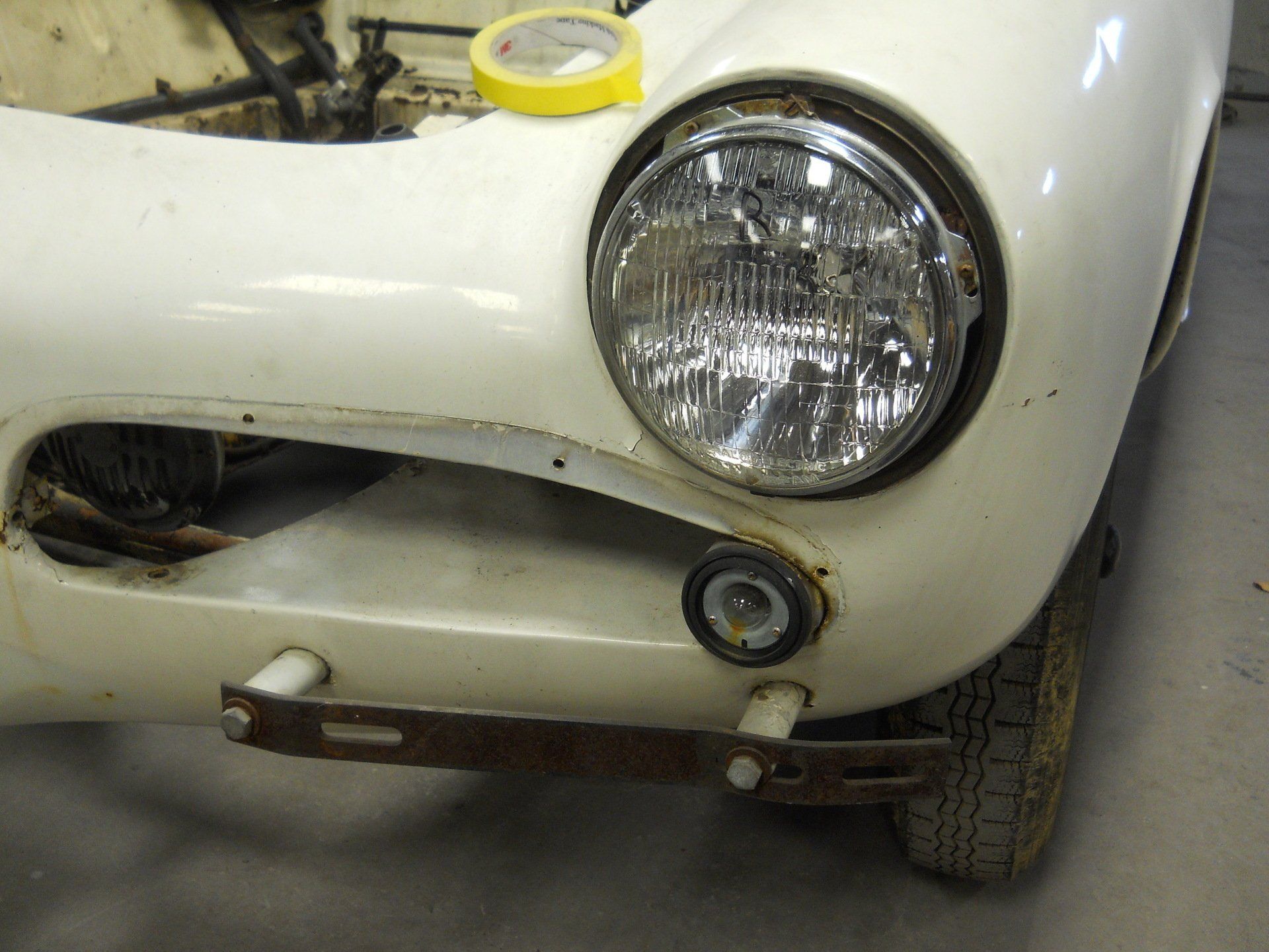 White vintage car front with headlight and turn signal detail. Rust on bumper and surrounding body.