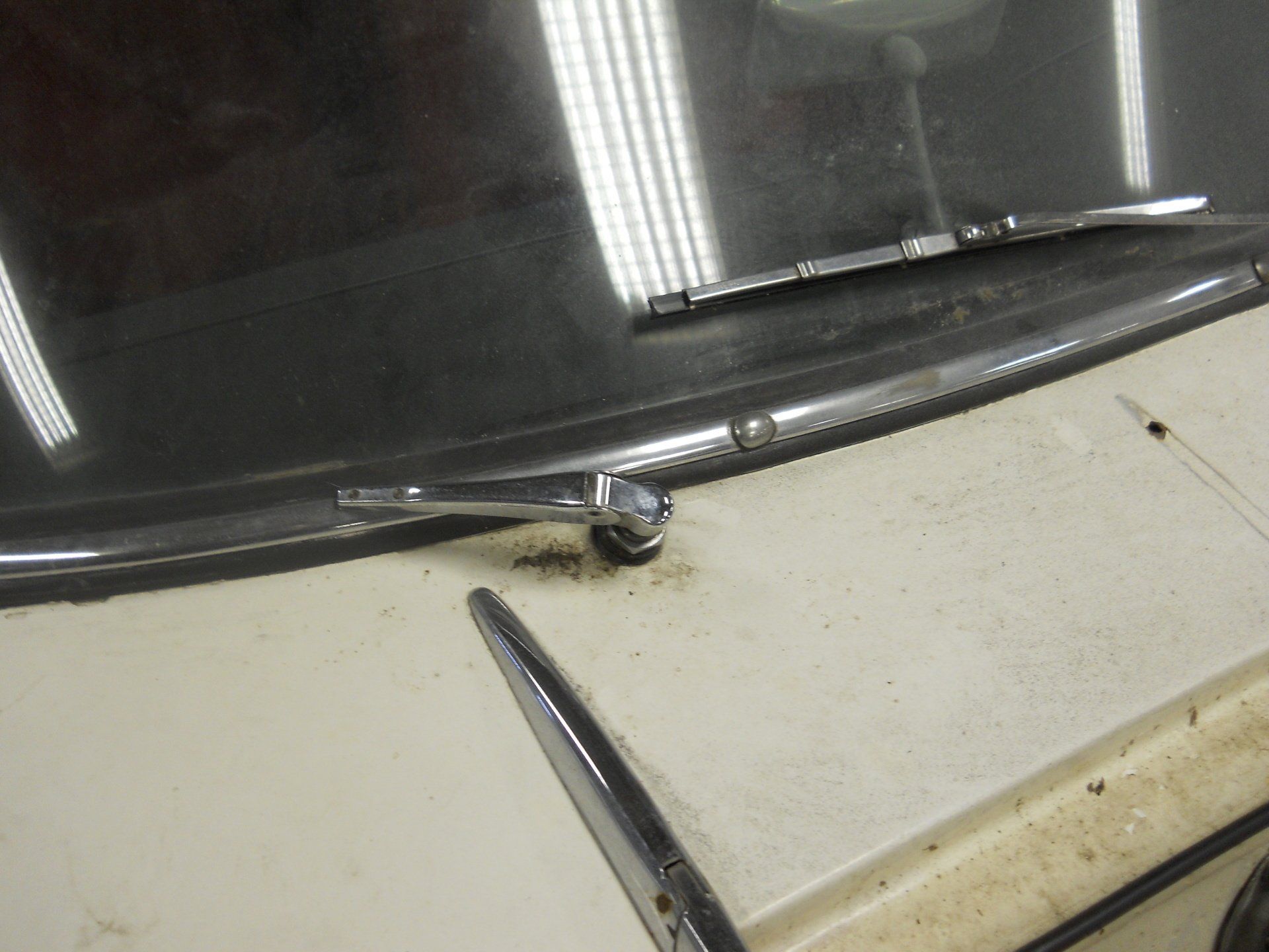 Windshield wiper on a light-colored car. Chrome wiper blades, weathered hood.