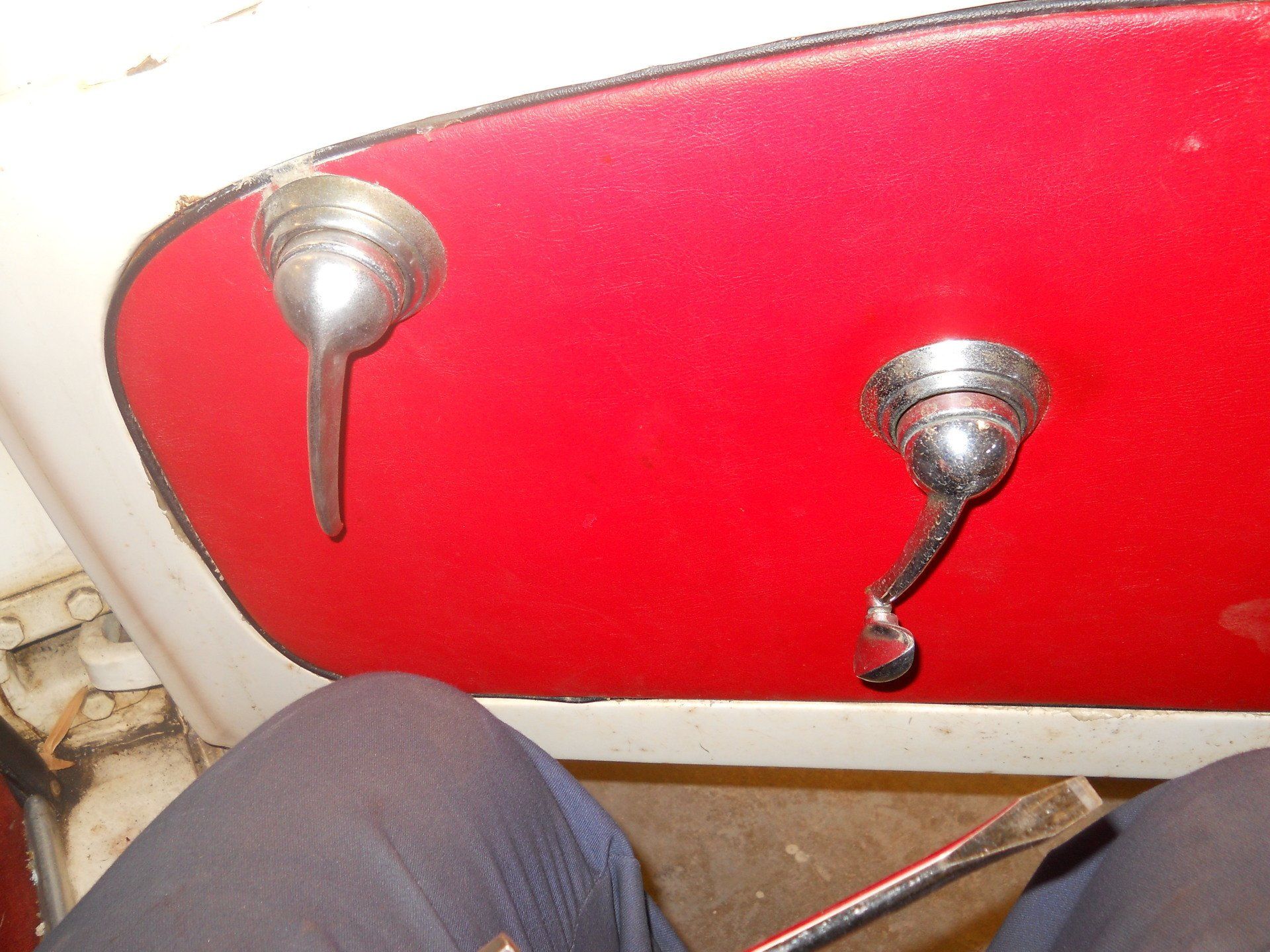 Red car door panel with two silver handles. A person's lap and a screwdriver are visible.