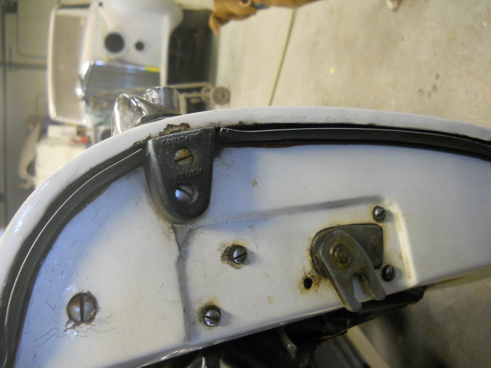 Close-up of a white boat's metal components with a black rubber seal, showing bolts and hardware.