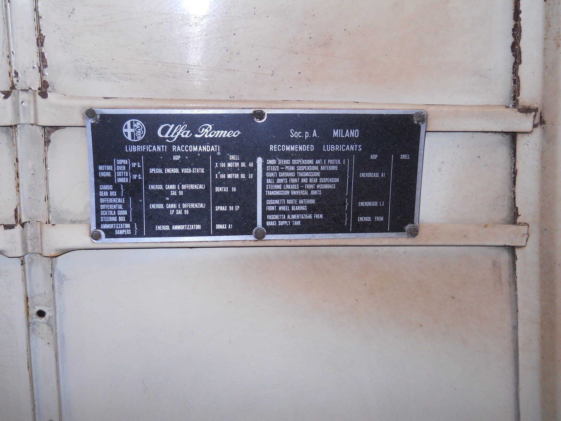 Black and silver Alfa Romeo information plate attached to a cream-colored surface with visible bolts.