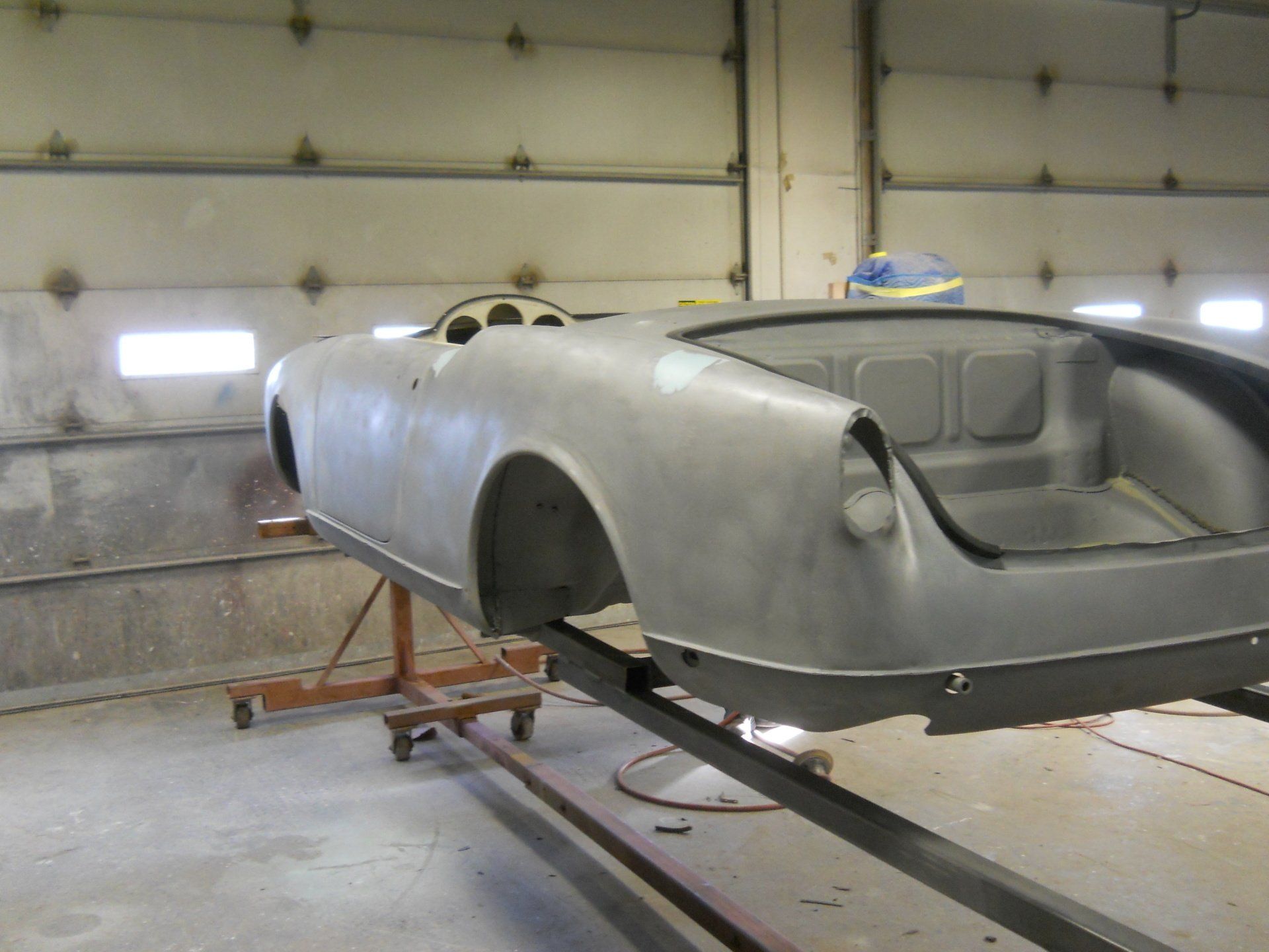 Gray sports car body in a workshop, mounted on a stand.