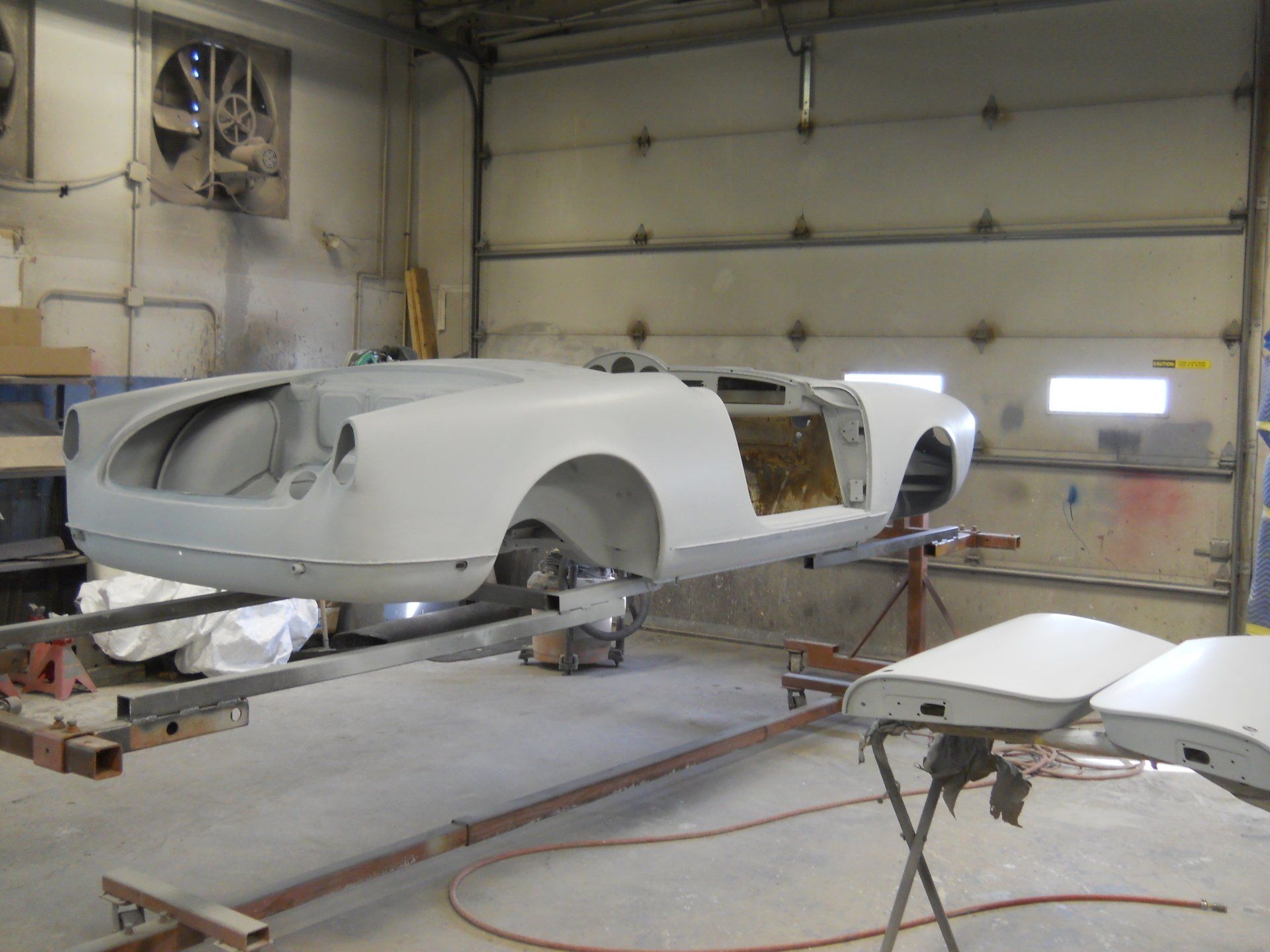 Car body in primer, mounted on a rack in a garage.