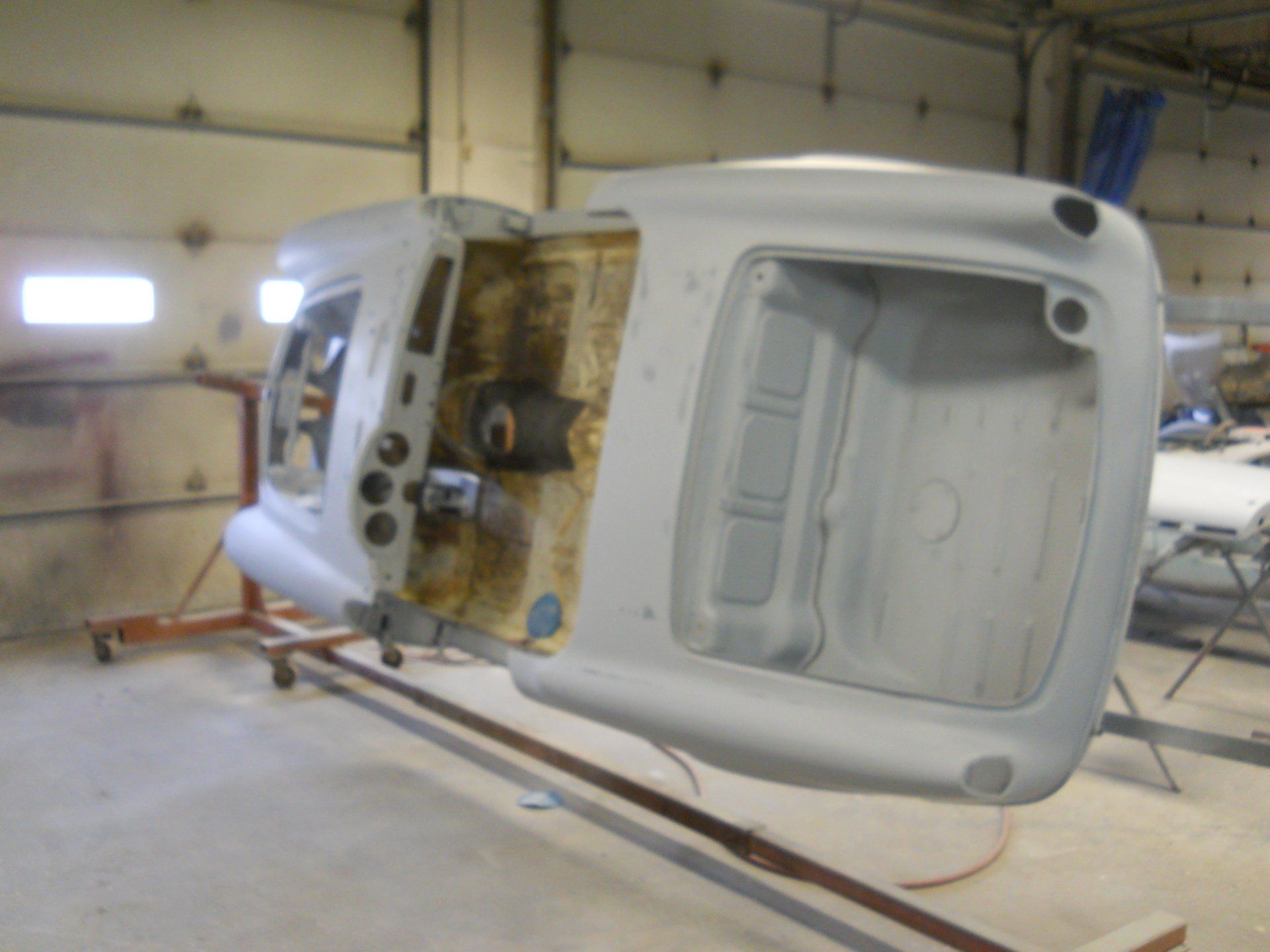 Gray car body on a rotisserie, inside a workshop. Underside exposed.
