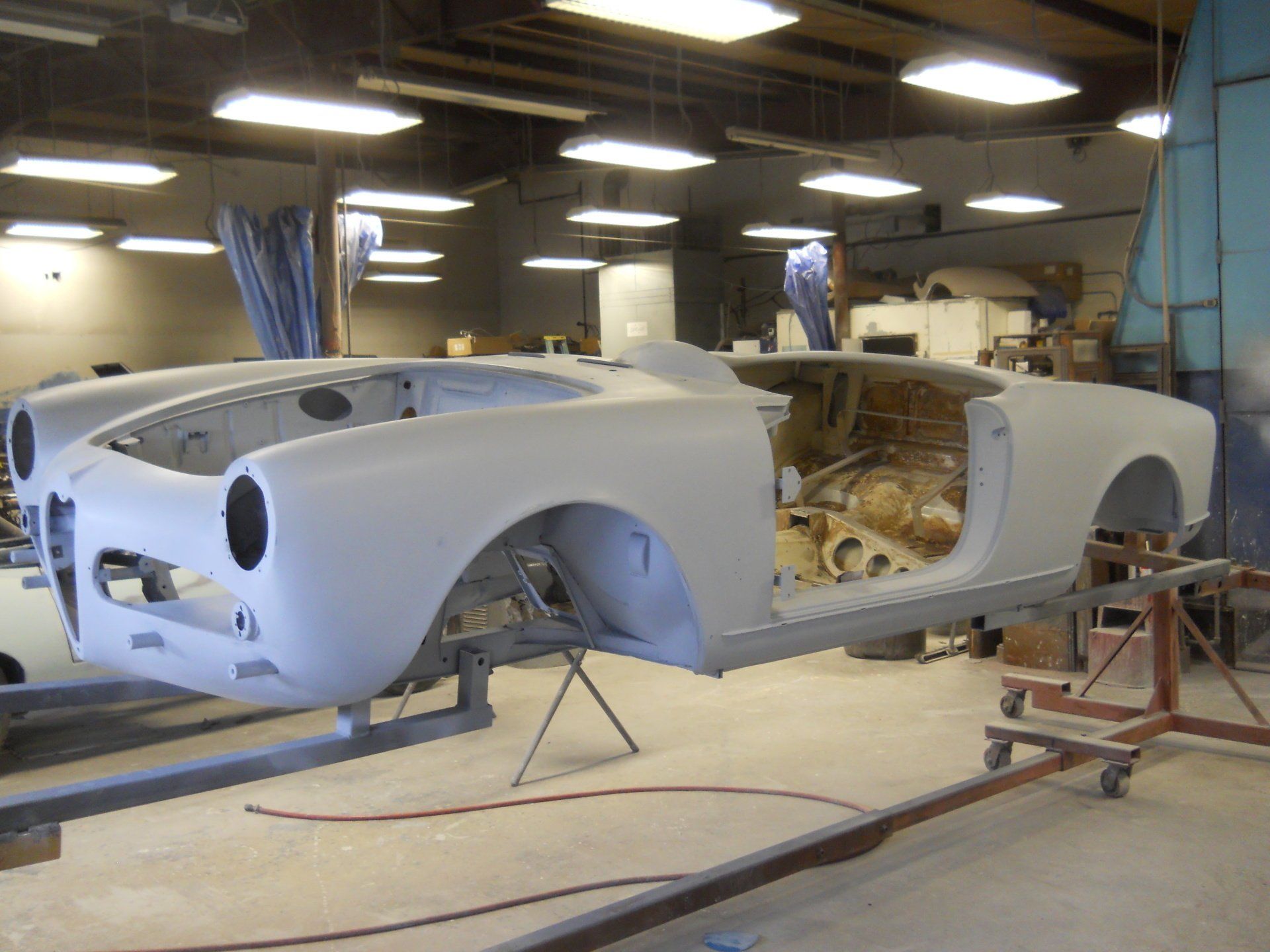 Classic car body shell in primer, on a lift, inside a workshop.