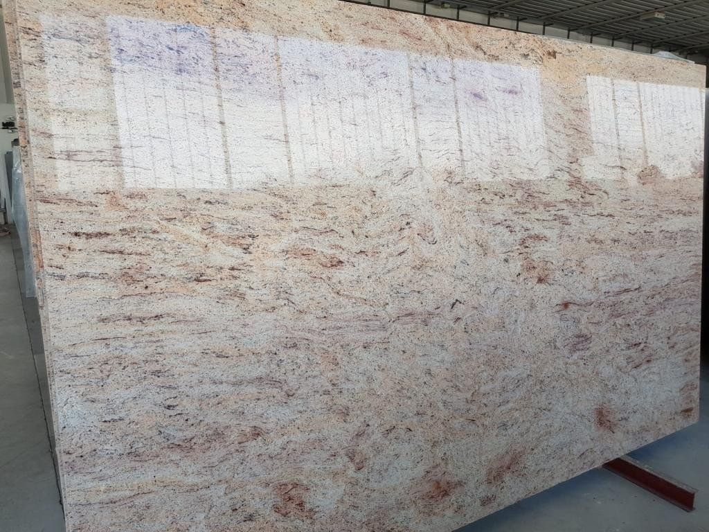 Una grande lastra di granito lucidato con uno sfondo color crema chiaro e motivi a spirale rosa, arancioni e grigi.