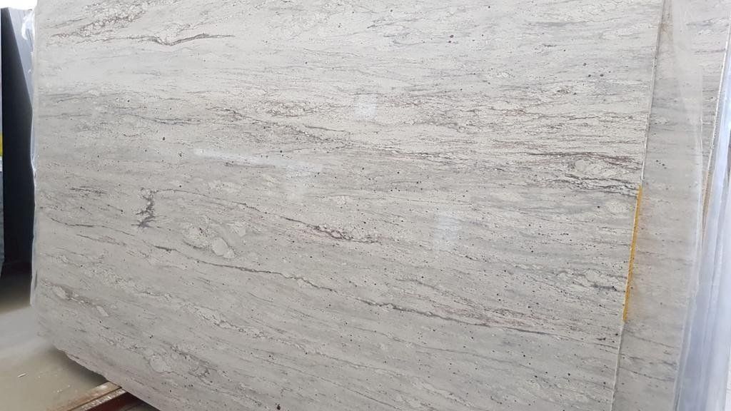 Una grande lastra di granito di colore bianco sporco, con sottili venature orizzontali grigie e macchie scure.