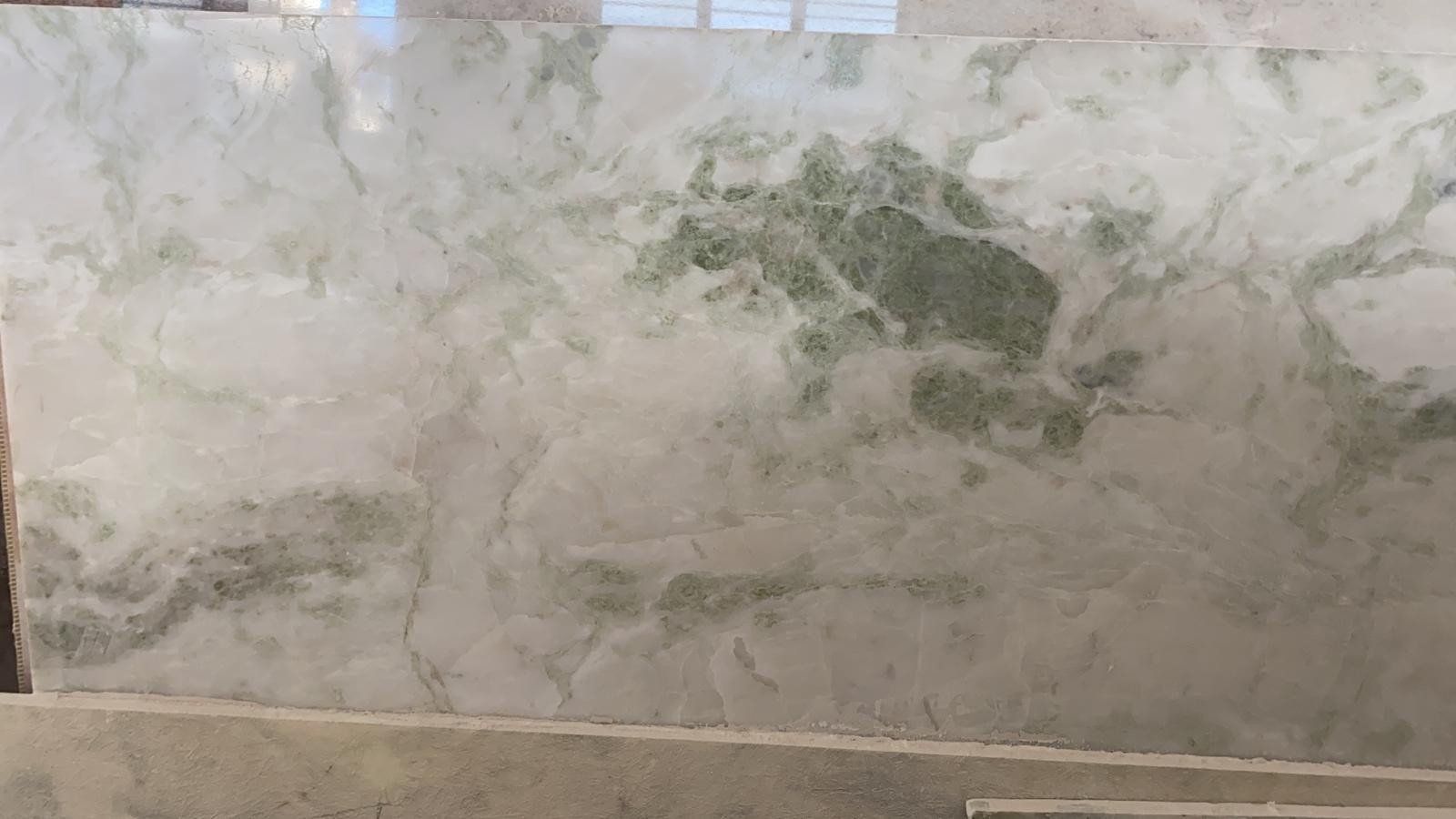 Una lastra di marmo bianco e grigio caratterizzata da venature e motivi a spirale di un verde salvia intenso e ben visibili.