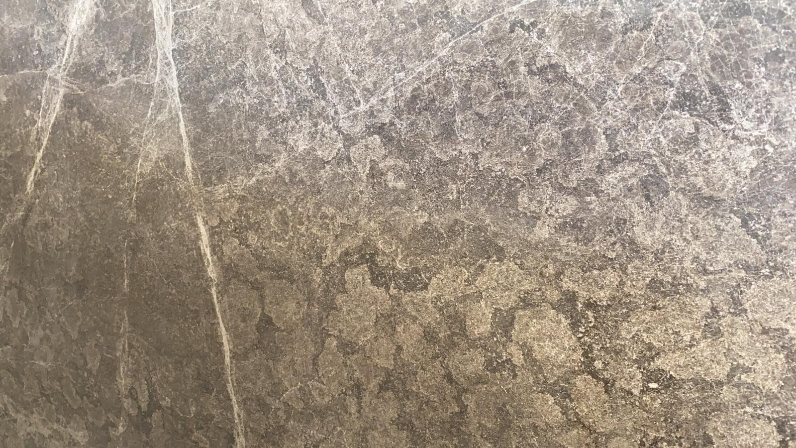 Primo piano di una lastra di marmo marrone scuro con venature irregolari di colore chiaro che percorrono tutta la superficie.