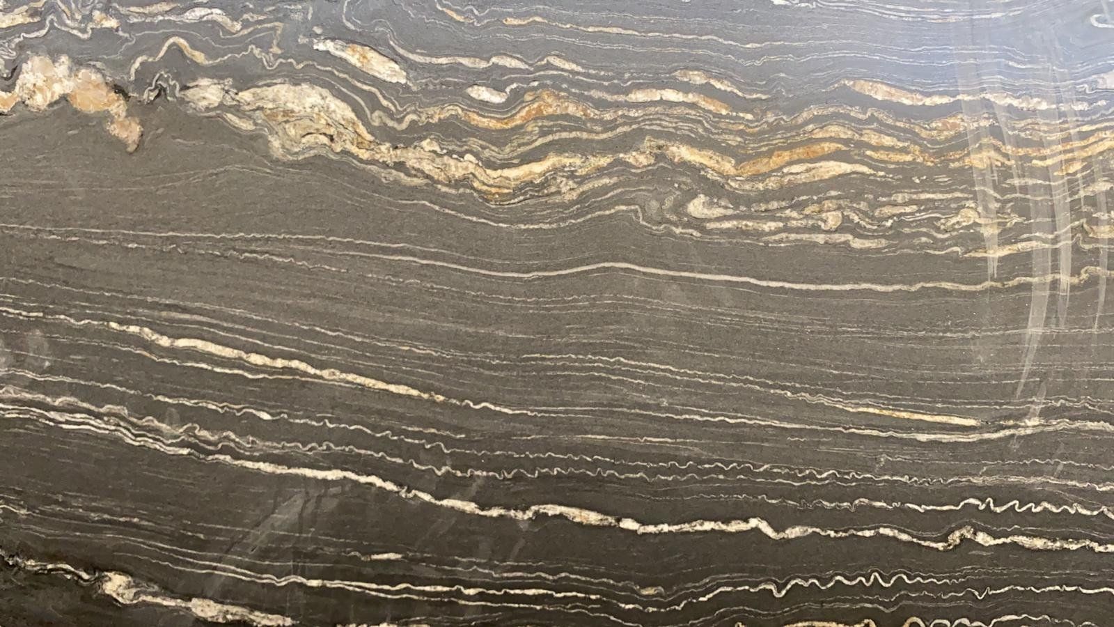 Primo piano di una lastra di pietra scura levigata con venature orizzontali ondulate di minerali bianchi, grigi e dorati.