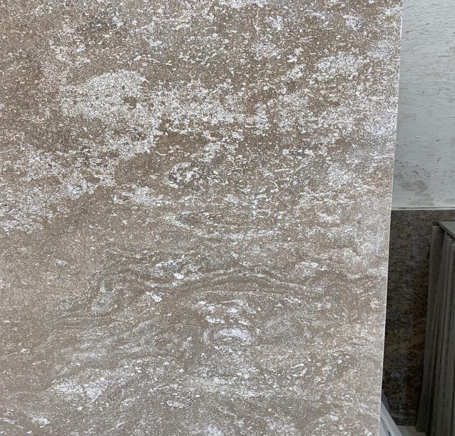 Primo piano di una lastra di pietra ruvida, di colore beige, con venature marmorizzate e sfumate nei toni del bianco e del marrone chiaro.