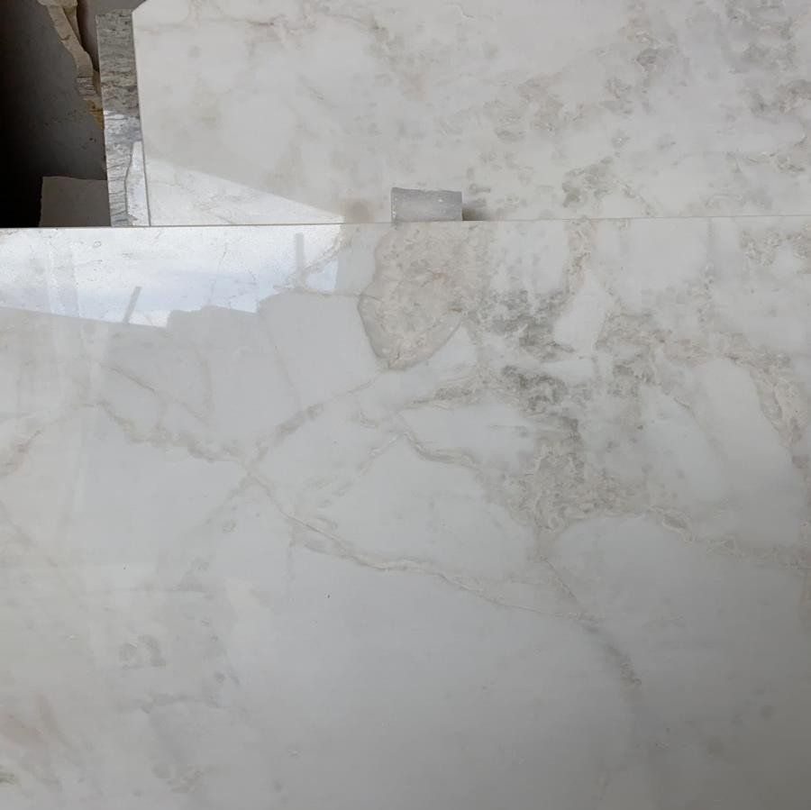 Vista ravvicinata di piastrelle di marmo bianco lucido con delicate venature beige e grigie, mostrate disposte a strati.