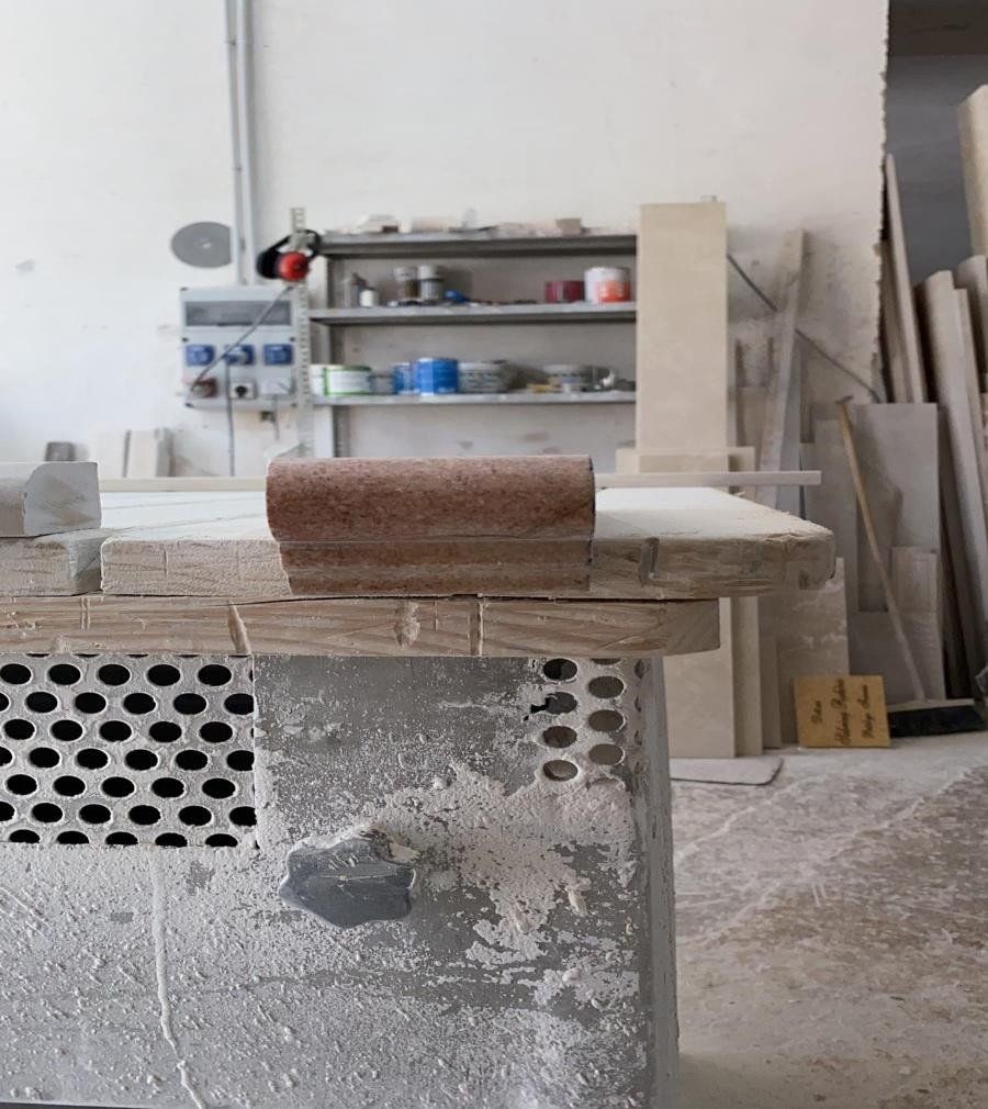 In un'officina, un primo piano mostra un banco da lavoro in legno con un pezzo arrotondato e ruvido di colore marrone rossastro fissato sul bordo.