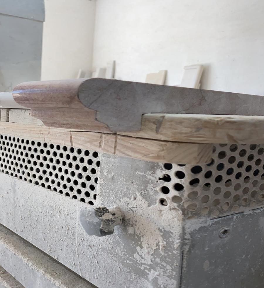 Una lastra di pietra chiara e levigata, con un bordo curvo e decorato, poggia su una base metallica grezza e perforata.
