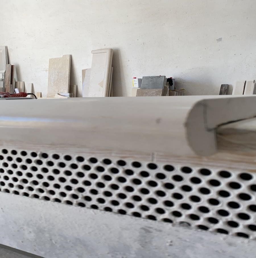 Primo piano di un bancone arrotondato di colore chiaro, sopra un pannello di rete metallica bianca, in un'officina.