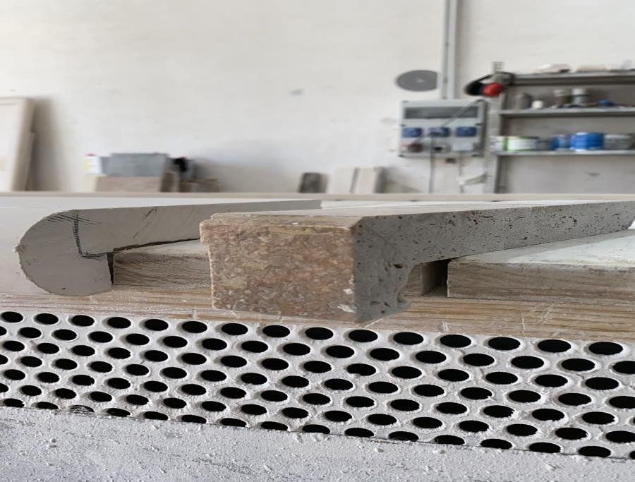 Primo piano di un gradino in pietra con superficie ruvida e bordo arrotondato, appoggiato su un banco da lavoro in officina.