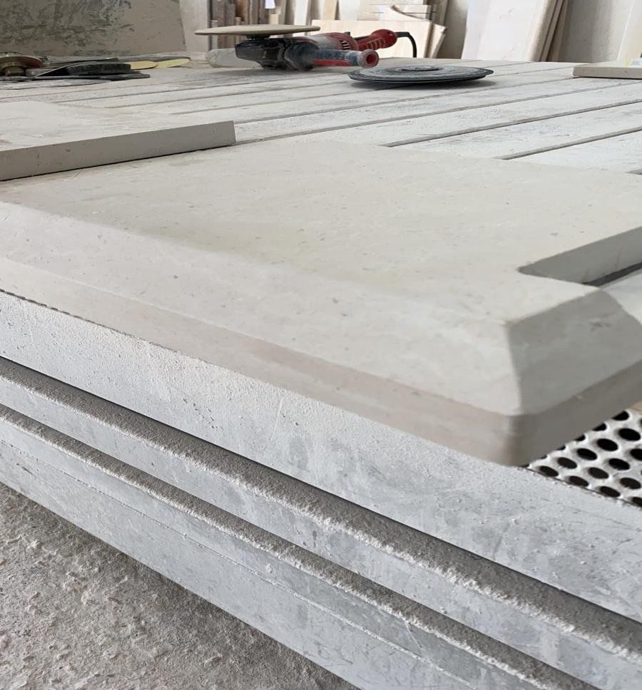 In un'officina, sullo sfondo si trovano una pila di lastre di pietra grigio chiaro, una delle quali con un bordo smussato.