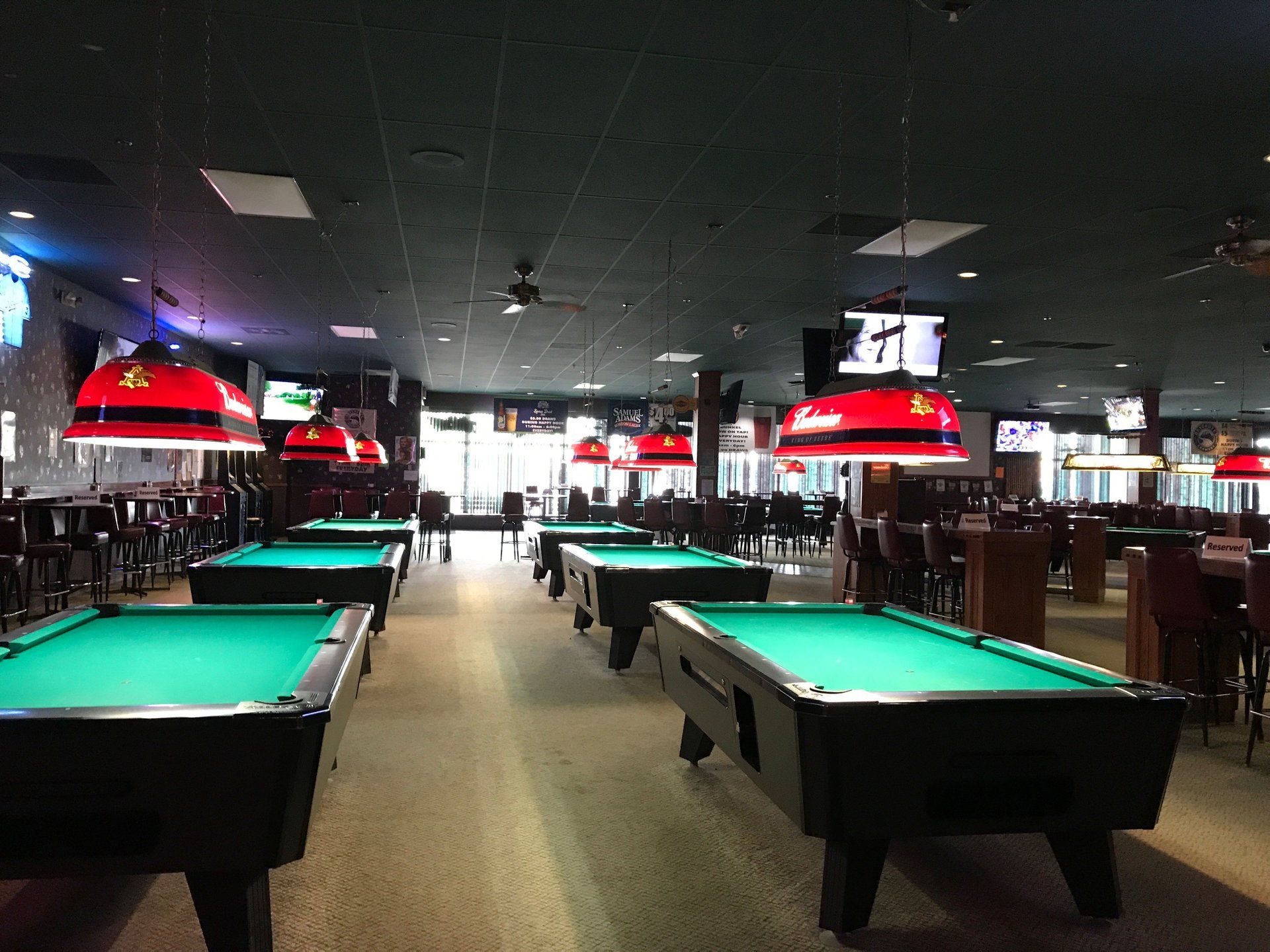 Empty pool hall with green felt tables and red hanging lights on a dark ceiling.
