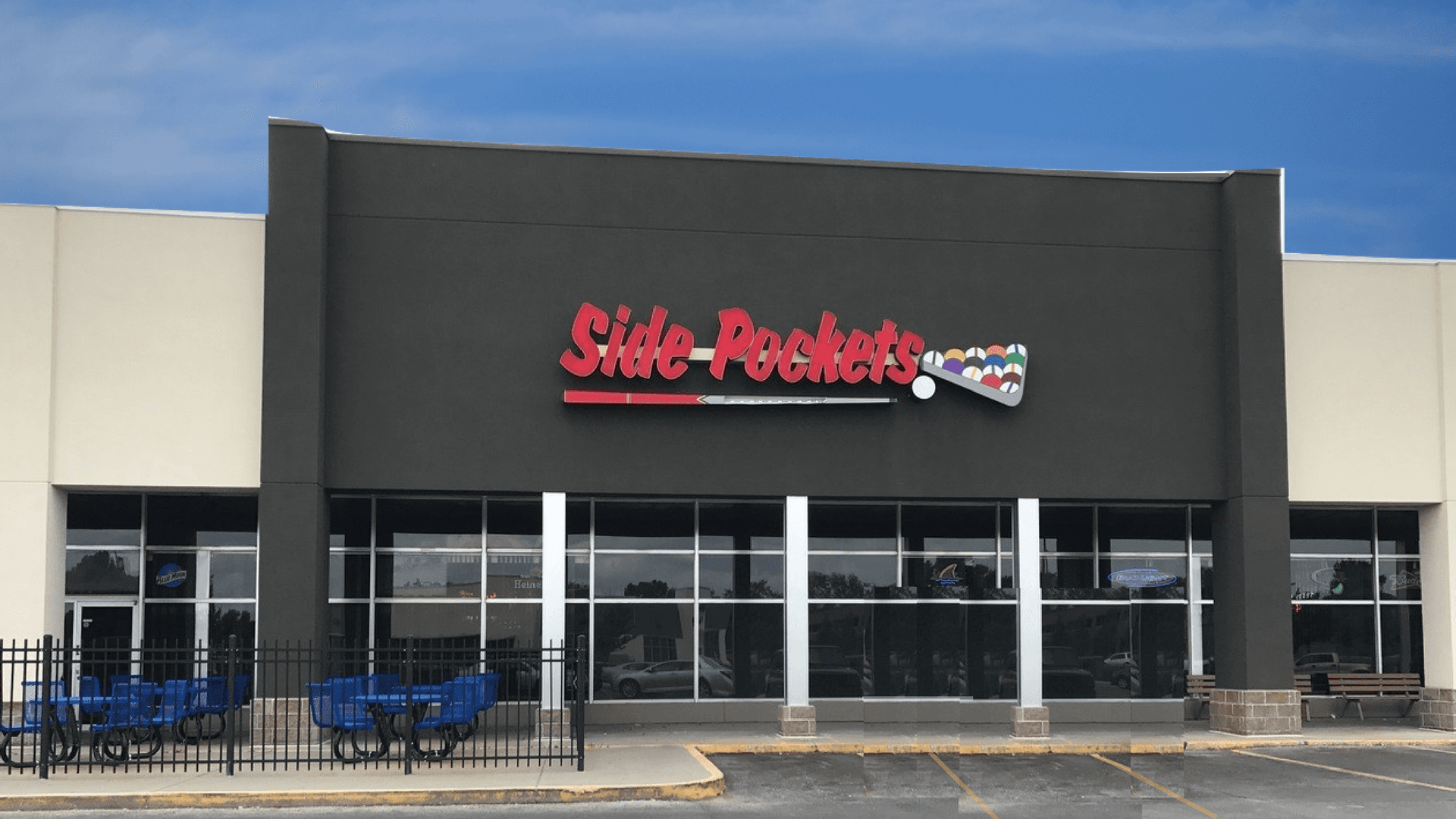 Side Pockets storefront with red sign on a dark facade and blue outdoor seating in front.