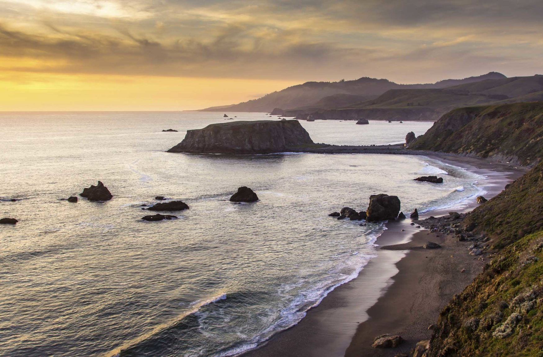 The sun beginning to set over the Pacific Ocean in a view looking down over Blind Beach and Goat Rock near Jenner in Sonoma County, Northern California.