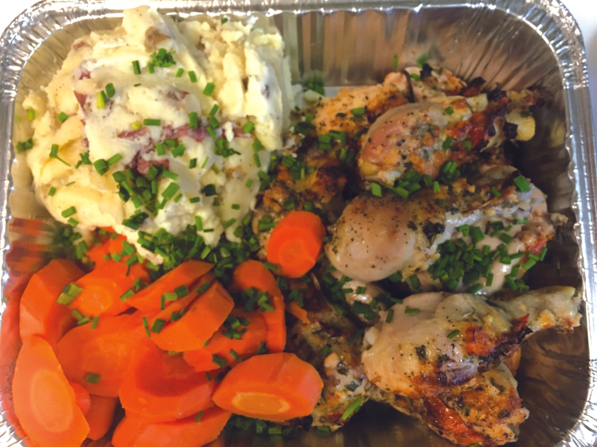A foil container filled with chicken carrots and mashed potatoes
