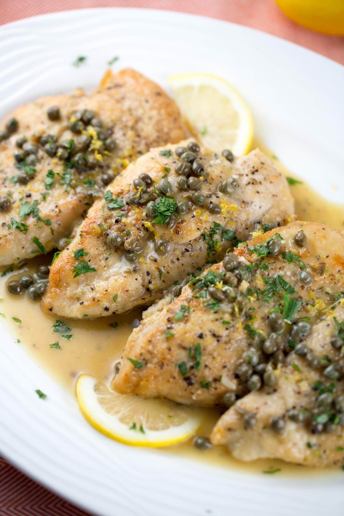 A white plate topped with chicken , capers and lemon slices.