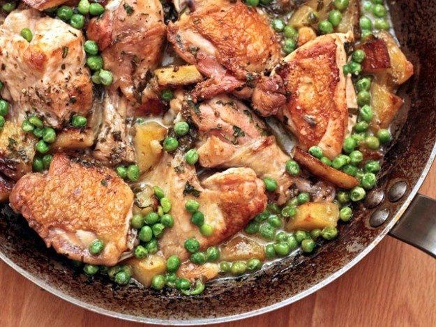 A pan filled with chicken , peas and potatoes on a wooden table.