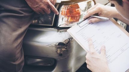 A person is writing on a clipboard in front of a car.