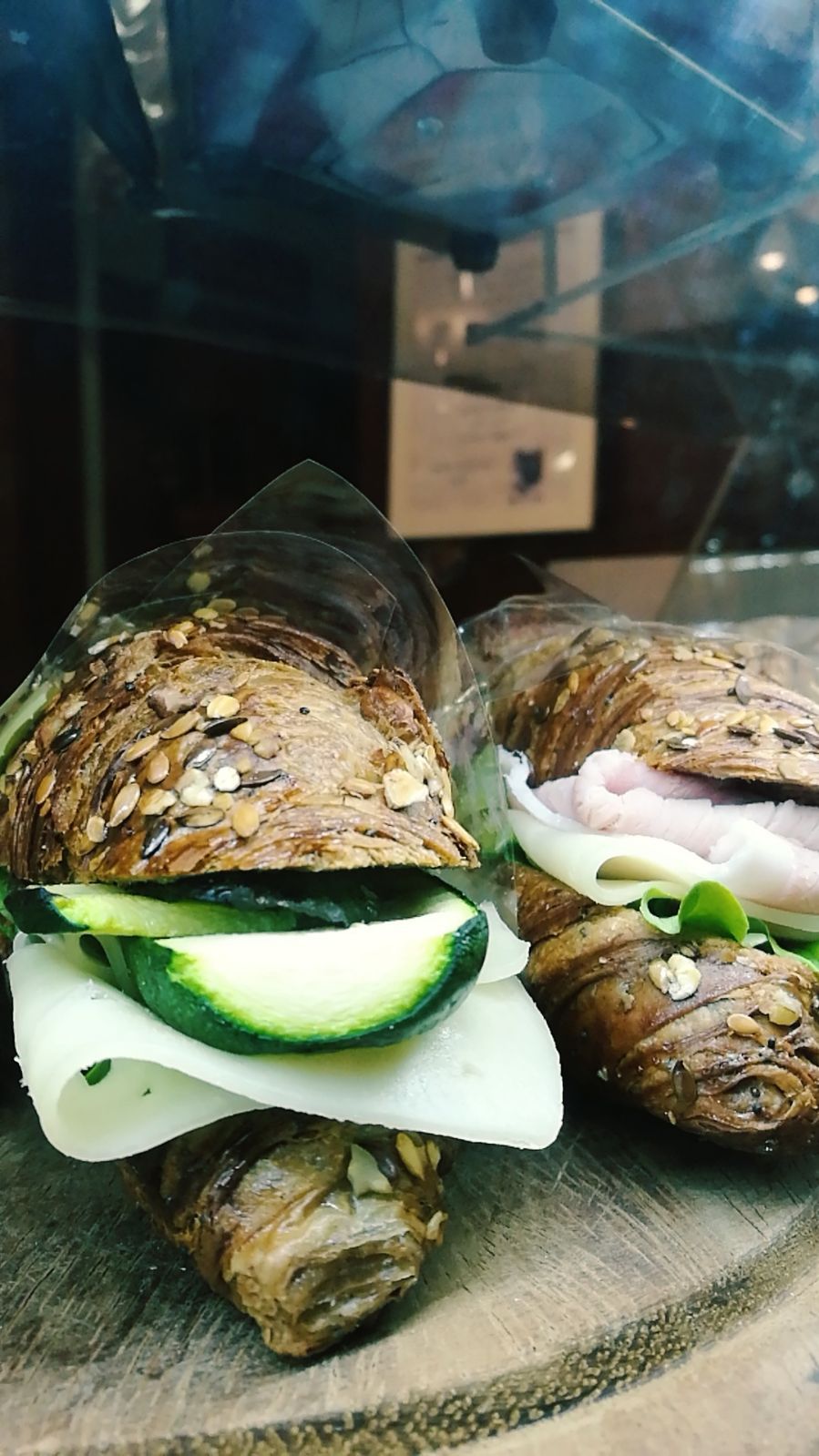 Due croissant su un tagliere di legno. Uno con zucchine e formaggio, l'altro con prosciutto, formaggio e verdure.