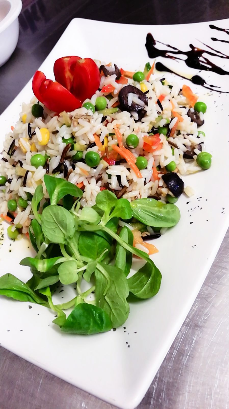 Piatto di riso con verdure, verdure a foglia verde e pomodoro su un piatto bianco, guarnito con glassa balsamica.
