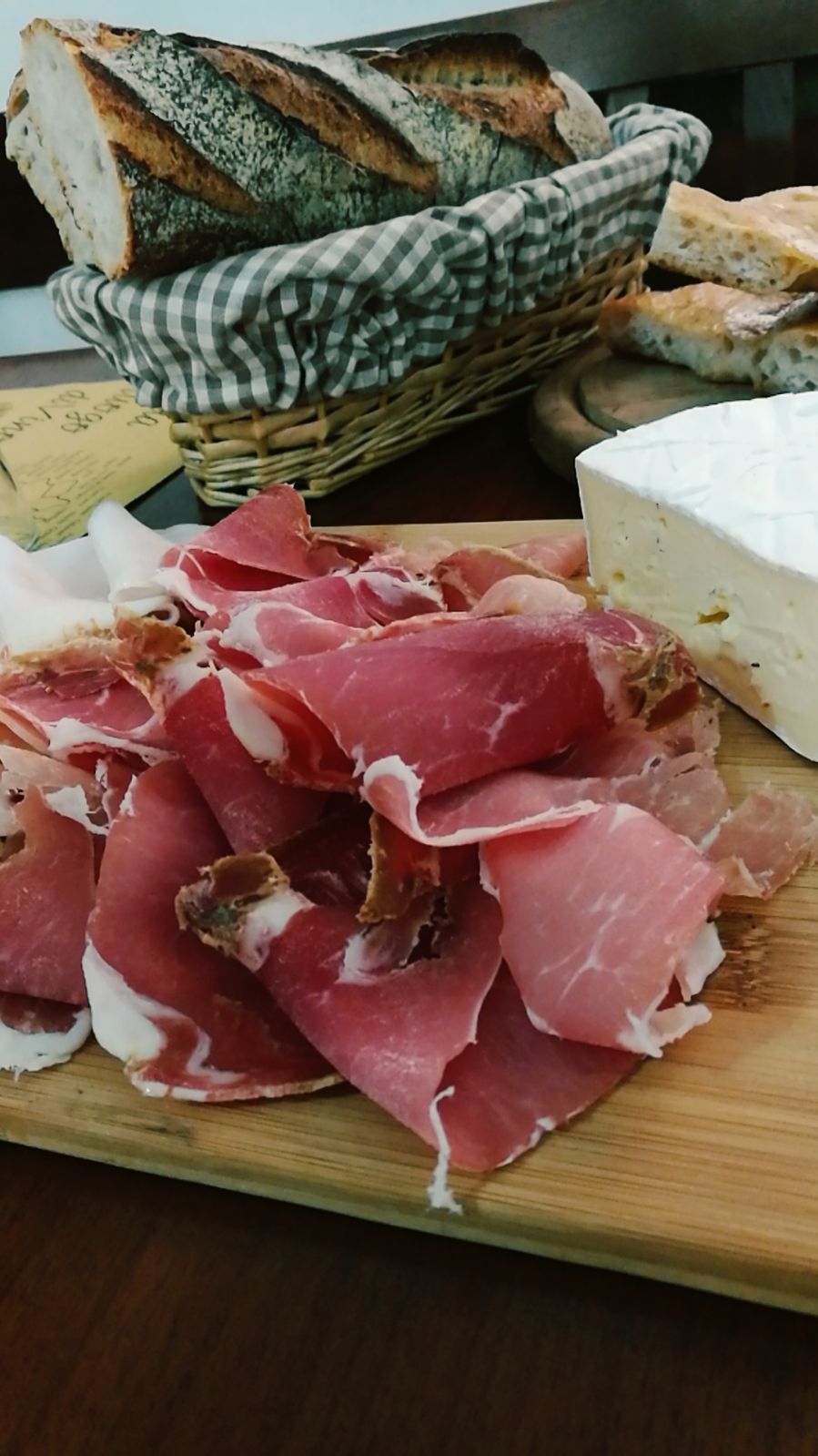 Tagliere di salumi: prosciutto affettato, brie, cestino di pane e focaccia.