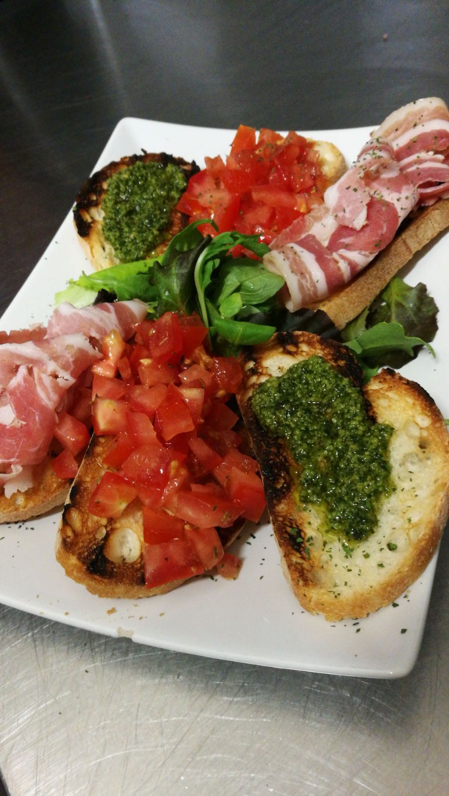 Piatto di bruschette: pane tostato con pomodoro, pesto e salumi; verdure fresche.