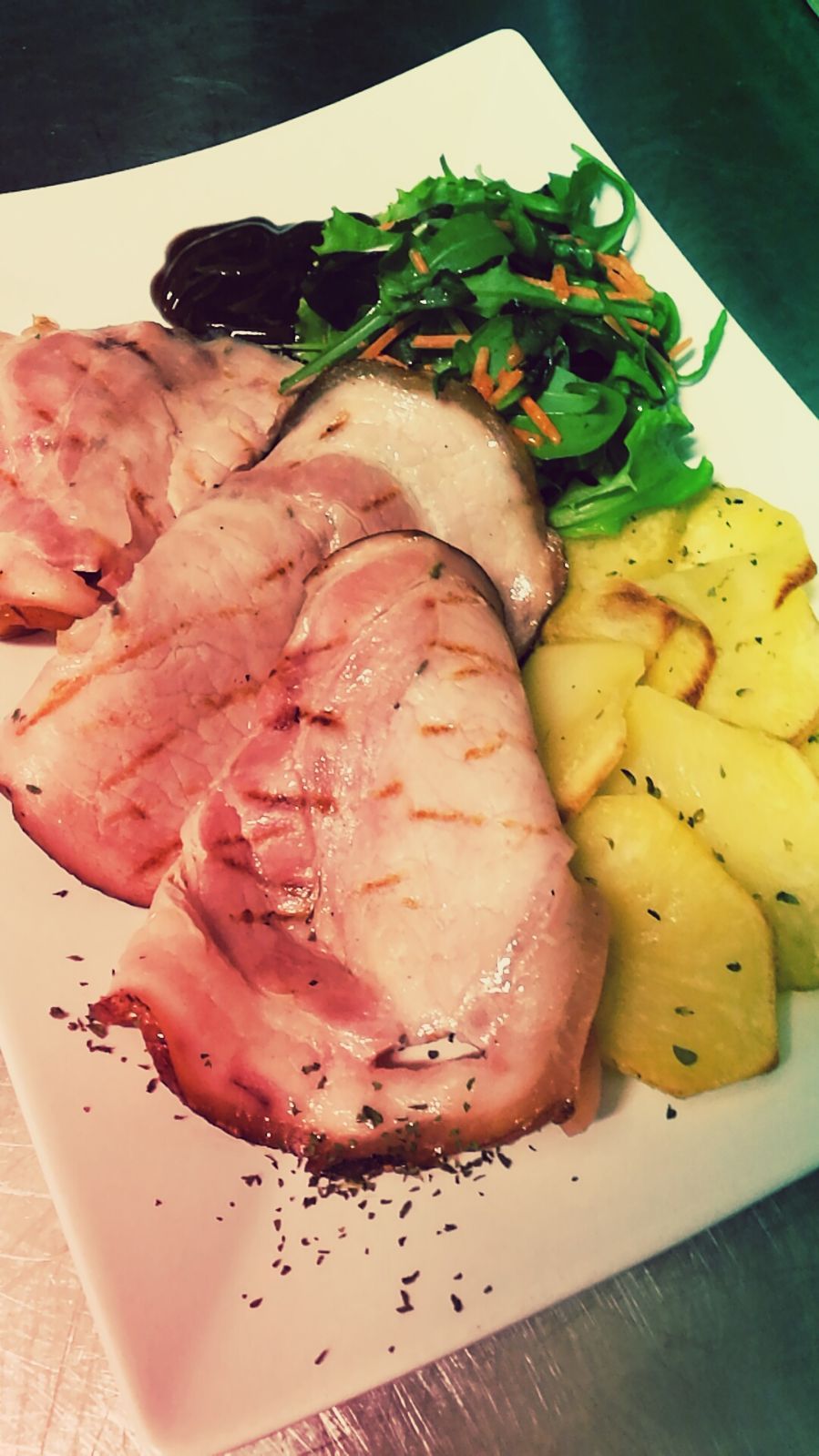 Fette di prosciutto grigliato con patate arrosto e verdure su un piatto bianco.