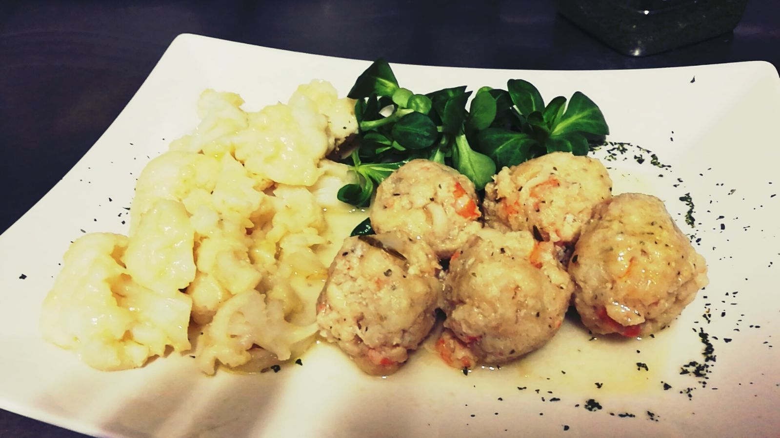 Piatto con polpette, cavolfiore e verdure; cibo su un piatto bianco.