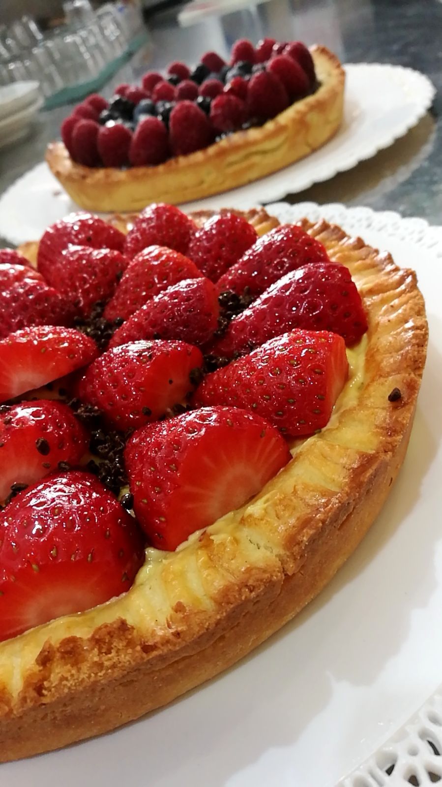 Due crostate di frutta, una alle fragole e una ai frutti di bosco, su centrini bianchi.