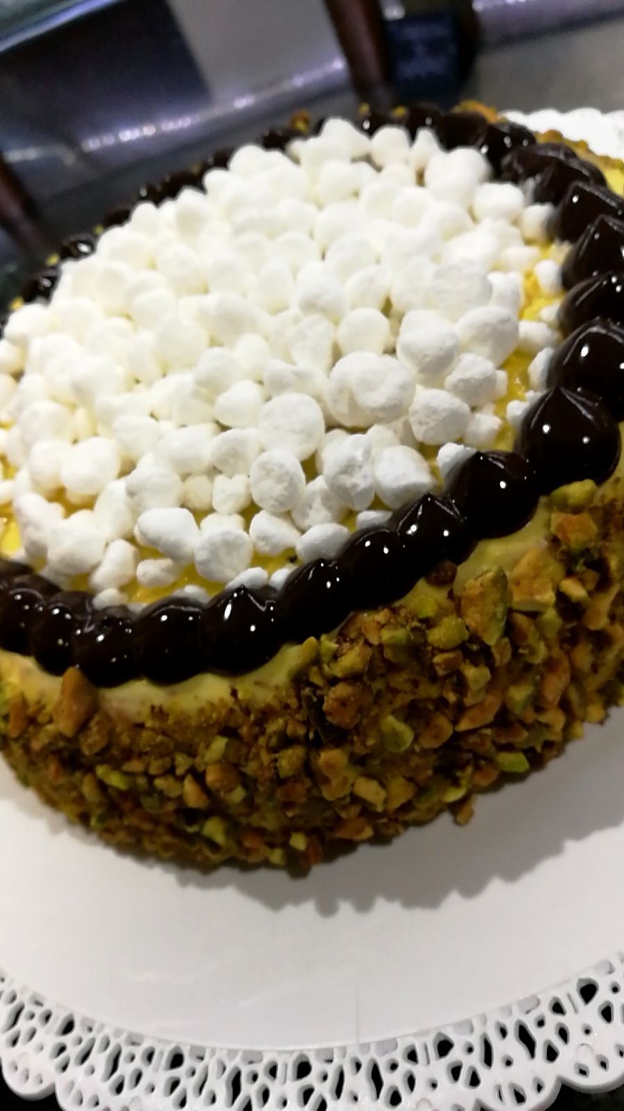 Torta con copertura di marshmallow bianco, bordo di cioccolato e base di pistacchio su un centrino.