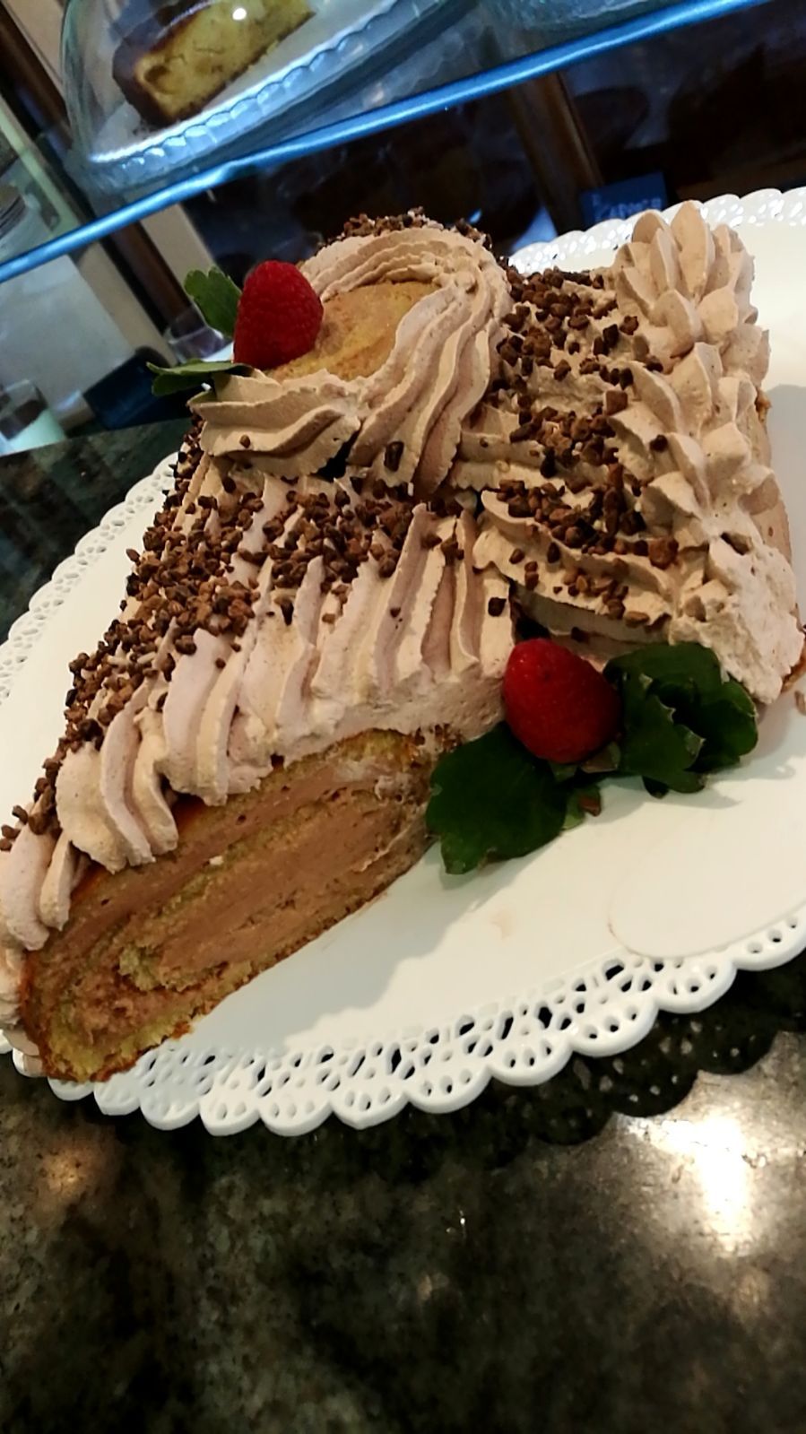 Tronchetto al cioccolato con glassa montata e guarnizione di lamponi, servito su un piatto con bordo in pizzo.