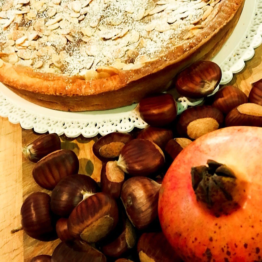 Crostata di castagne su centrino, circondata da castagne e un melograno.
