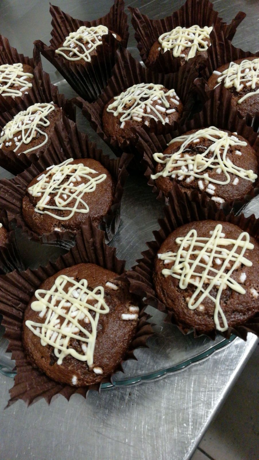 Cupcake al cioccolato in pirottini di carta marrone, ricoperti di glassa bianca, su un piatto di vetro.