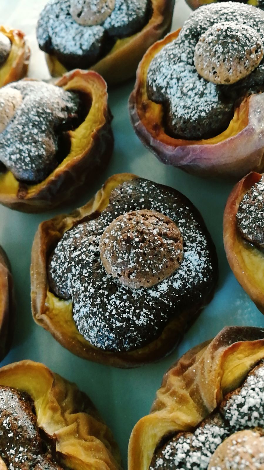 Primo piano di pasticcini cotti al forno con ripieno di cioccolato, ricoperti di zucchero a velo e un piccolo biscotto.