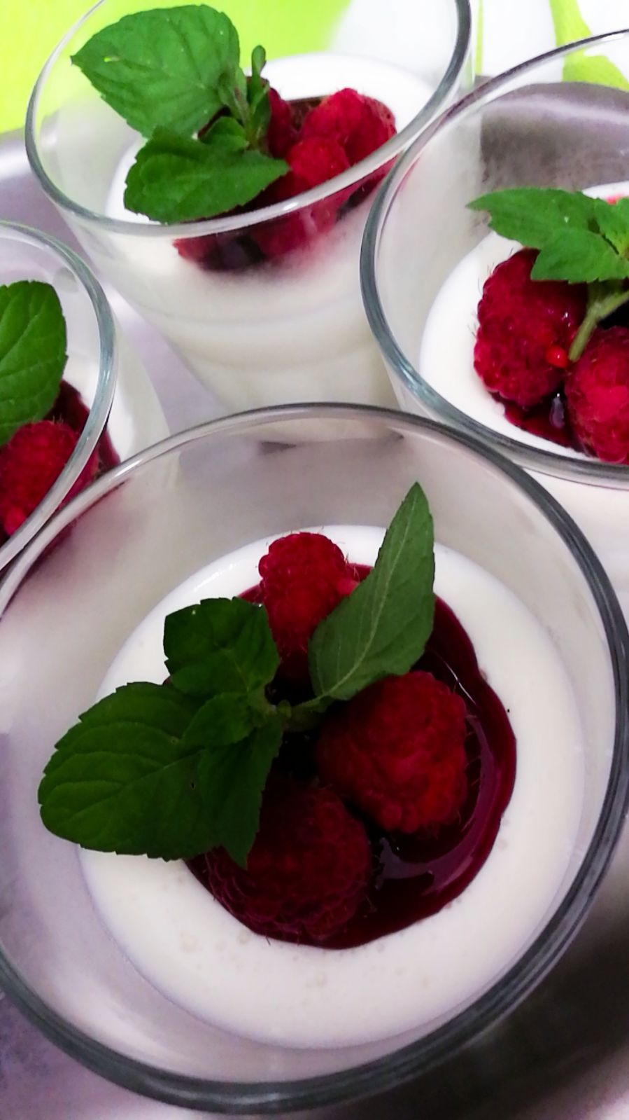 Dessert in piccole tazze di vetro: panna bianca, lamponi rossi, salsa di frutti di bosco e foglie di menta sopra.
