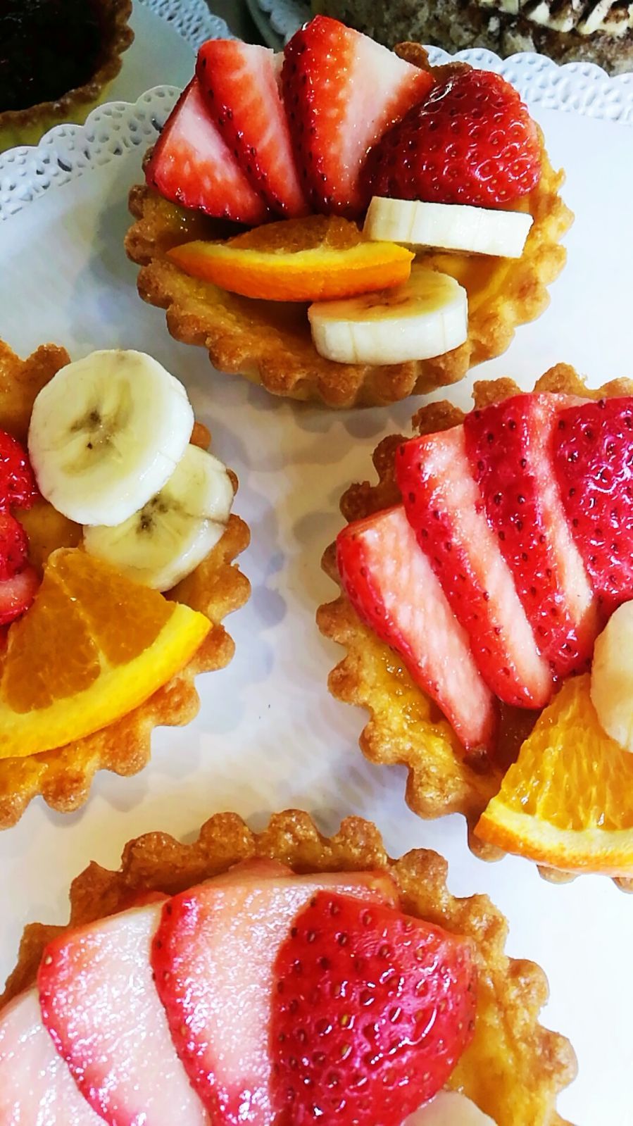Crostate di frutta: fette di fragola, banana e arancia disposte su gusci di pasta.