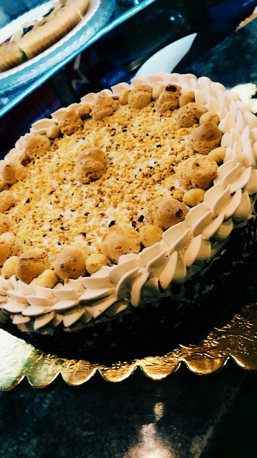 Torta con glassa alla crema, briciole commestibili e piccole decorazioni rotonde su un piatto dorato smerlato.