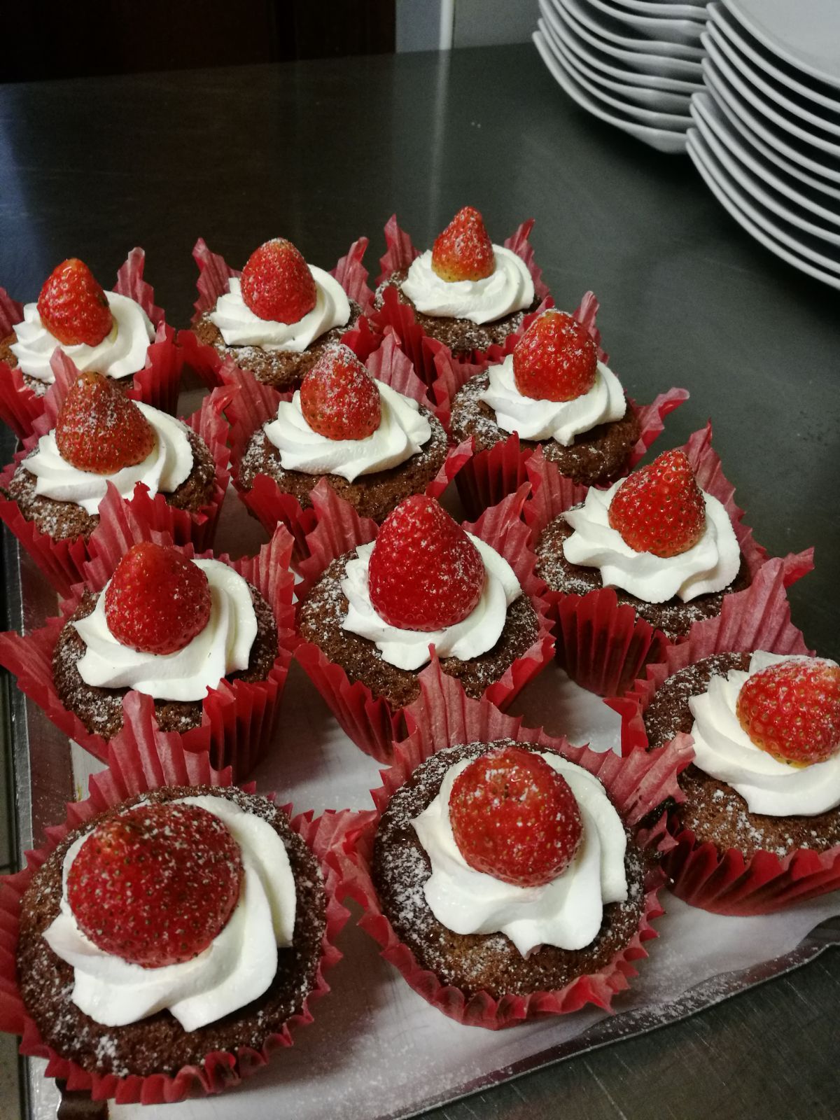 Cupcake al cioccolato con panna montata e fragole, disposti su un vassoio.