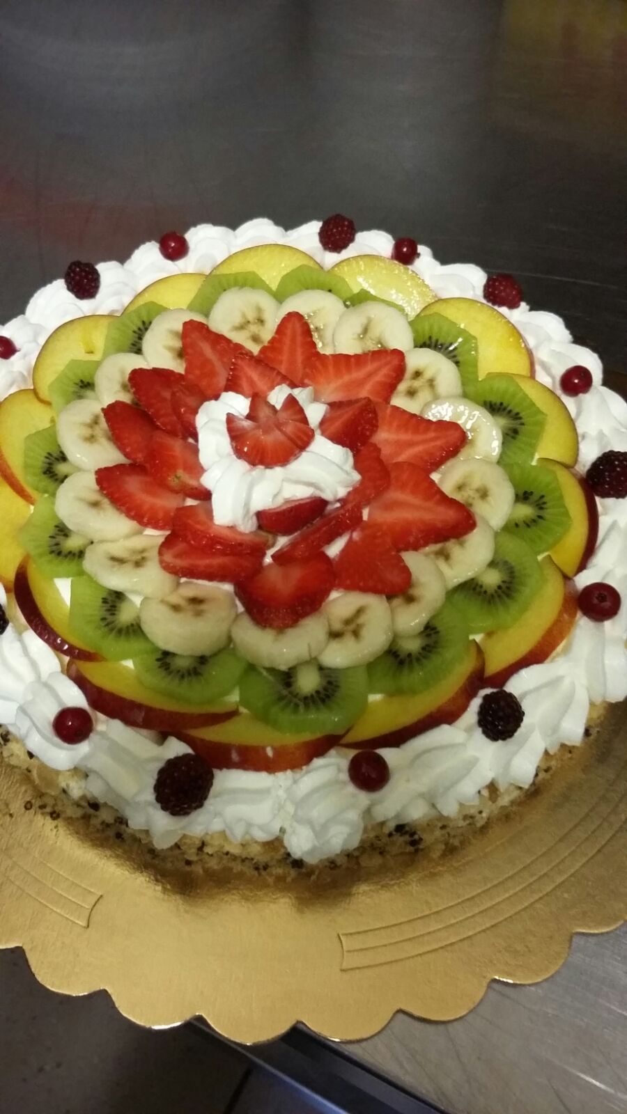 Crostata di frutta con fragole, kiwi, pesche e banane disposte su panna montata.