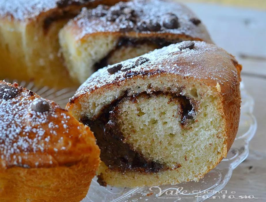 Pane arrotolato con ripieno di cioccolato, spolverato con zucchero a velo e gocce di cioccolato.